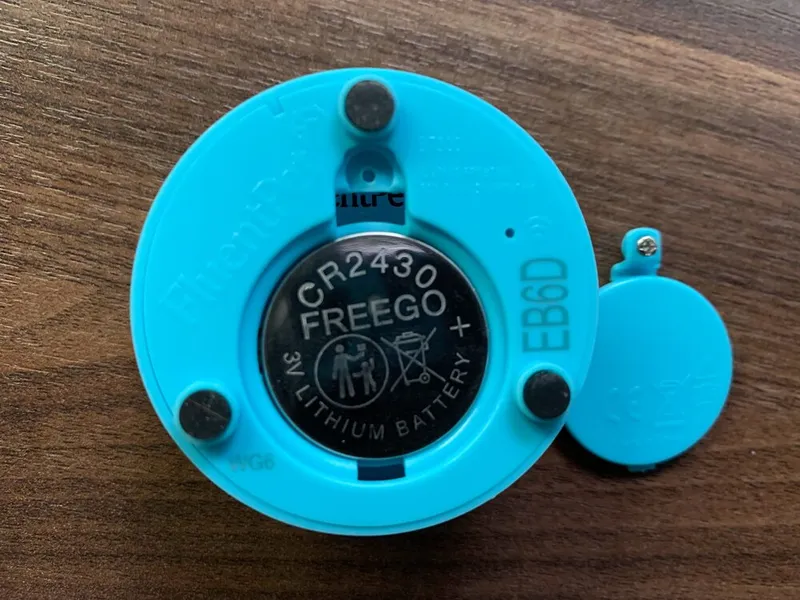 A Connect Button with its battery cover removed, showing a CR2430 coin battery with the + side facing out.